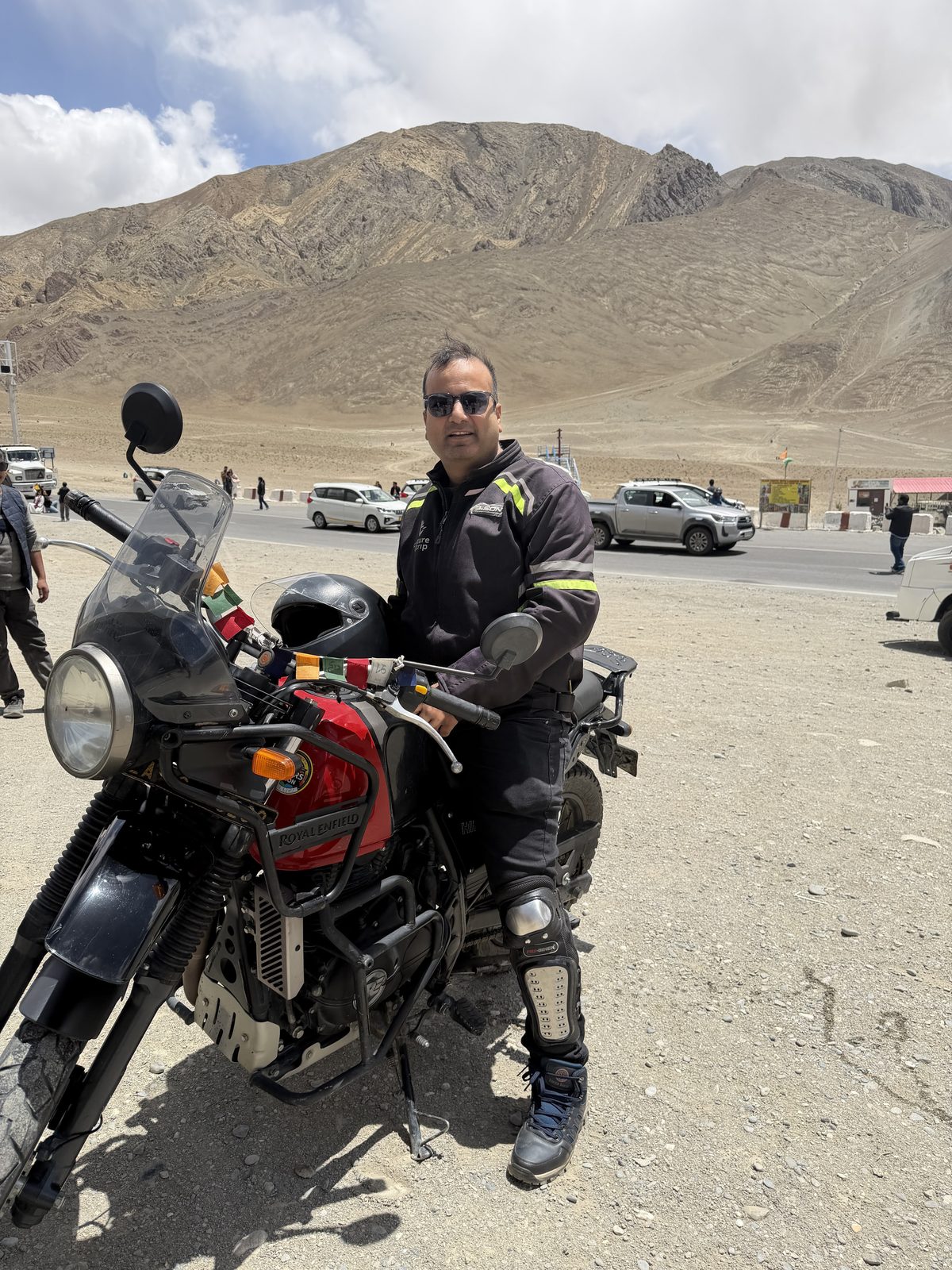 Sandeep Jain with his Royal Enfield motorcycle on a Ladakh road trip, mountains in the background